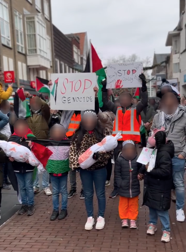 Een groep mensen, met voorop een rij kinderen, draagt Palestijnse vlaggen, keffiyeh en houden borden omhoog met teksten waaronder 'Stop genocide'.