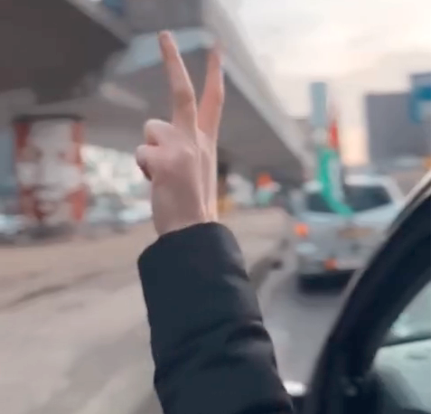 Een rij met auto's met Palestijnse vlaggen rijdt langs een viaduct met daarop een schildering met een gezicht van Nelson Mandela. De bestuurder van de meest dichtsbijzijnde auto maakt vanuit diens raam een V-teken voor overwinning.