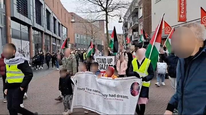 Een groep mensen marcheert door een stadscentrum. Zij dragen Palestijnse vlaggen. Voorop loopt een groep kinderen met een spandoek, met daarop de tekst (in het Engels): 'Zij hebben namen. Zij hadden dromen', plus de namen van duizenden mensen die door de zionistische bezetter vermoord zijn.
