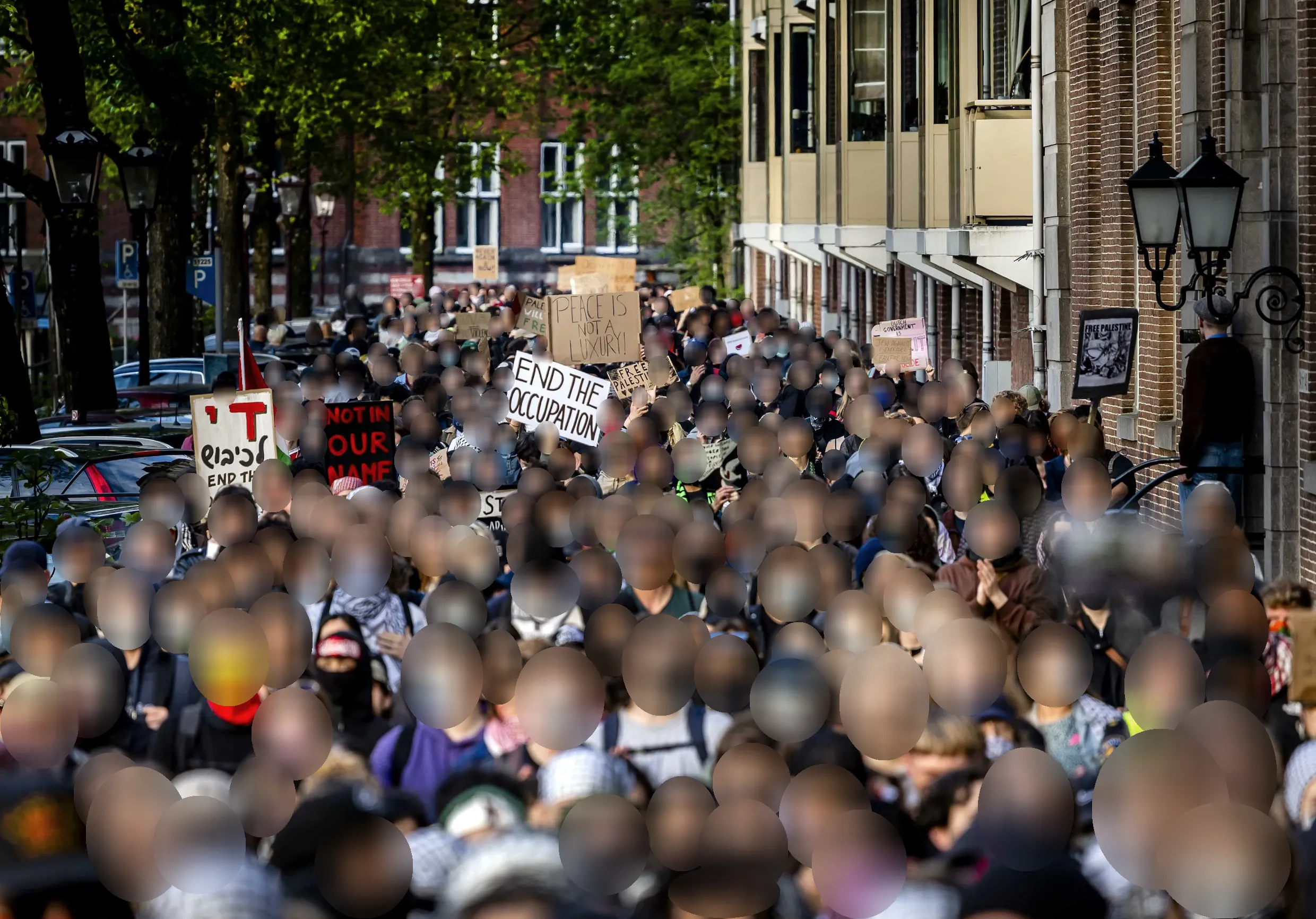 Een menigte van duizenden demonstranten marcheert door een stadsstraat. De demonstranten dragen borden met boodschappen zoals 'Beëindig de bezetting' en 'Niet in onze naam'. Vele dragen gezichtsmaskers. Het is een lichte, droge dag en de bomen aan de straat zijn groen.