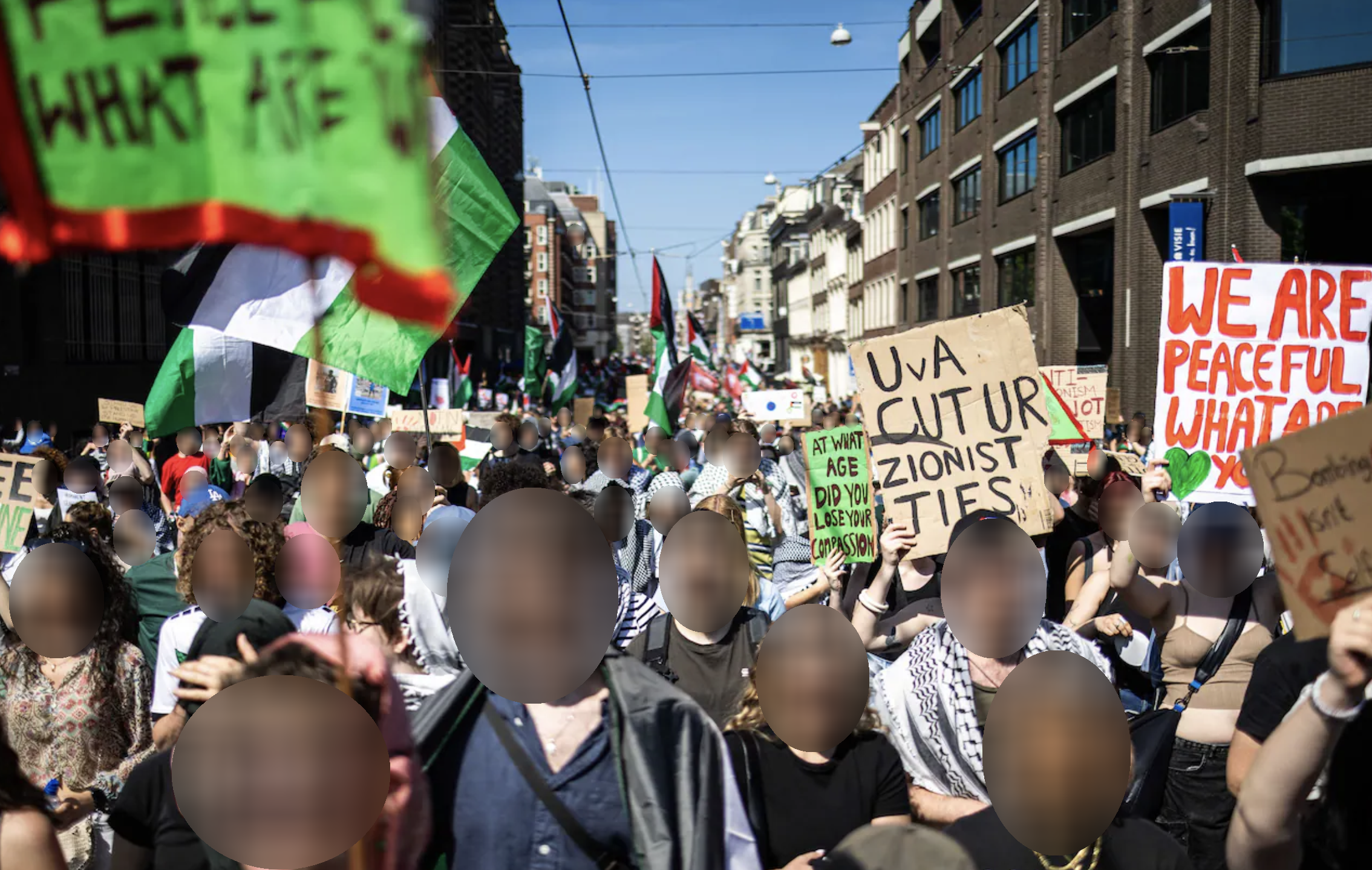 Een zee van duizenden mensen loopt met borden, spandoeken en Palestijnse vlaggen door een straat, op een heldere, zonnige dag. Velen van hen dragen keffiyeh. De demonstranten zingen of scanderen. Op de borden staan boodschappen (vaak in het Engels) zoals: 'UvA verbreek je zionistische banden', 'Wij zijn vreedzaam wat zijn jullie'.