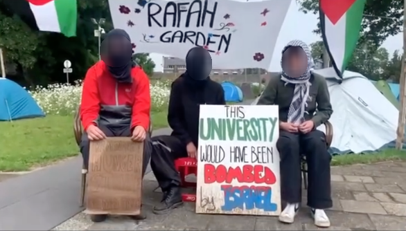 Drie mensen zitten op een binnenplaats en kijken recht in de camera. Voor hen staat een bord met daarop de tekst (in het Engels) 'Deze universiteit zou door Israël gebombardeerd zijn', en nog een ander bord. Achter hen hangt een spandoek met daarop de tekst (in het Engels) 'Rafahtuin' en een Palestijnse vlag. In de achtergrond staan op een grasveld verschillende tenten.