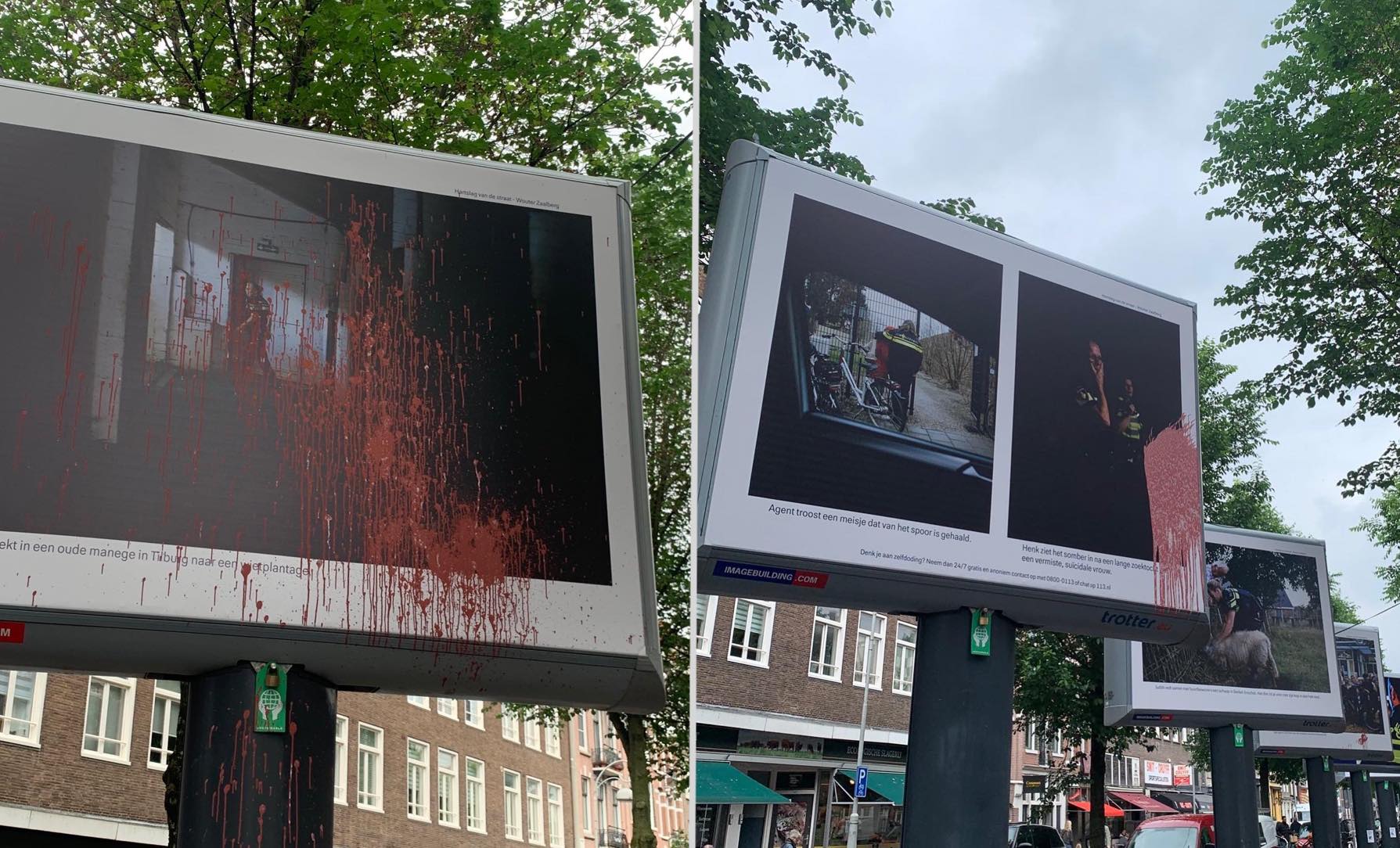Zicht op een straat in een gemengde wijk met wonen en marktstalletjes, met auto's en bomen, op een grauwe dag. Centraal in beeld staat een rij metershoge advertentieborden, met daarop propaganda voor de politie in de vorm van foto's en bijschrijf. Verschillende borden zijn met rode verf beklad.