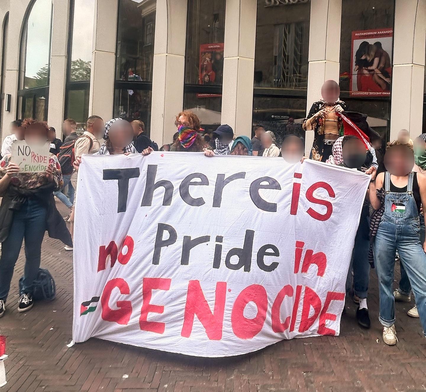 Ongeveer twintig mensen staan rondom een groot spandoek met daarop de tekst (in het Engels): 'Er is niks om trots op te zijn in genocide', met daarop ook een Palestijnse vlag.
