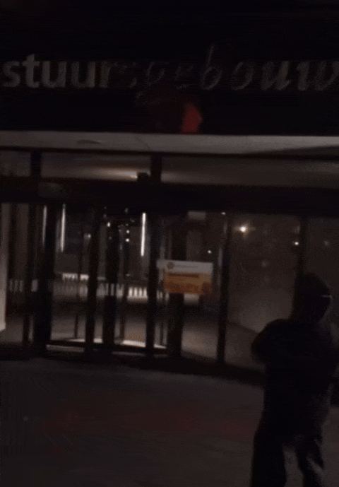 Nachtaanzicht op de voorgevel van het Bestuursgebouw van de Universiteit Utrecht. Een donker gekleed persoon werpt rode verf op de voorgevel.