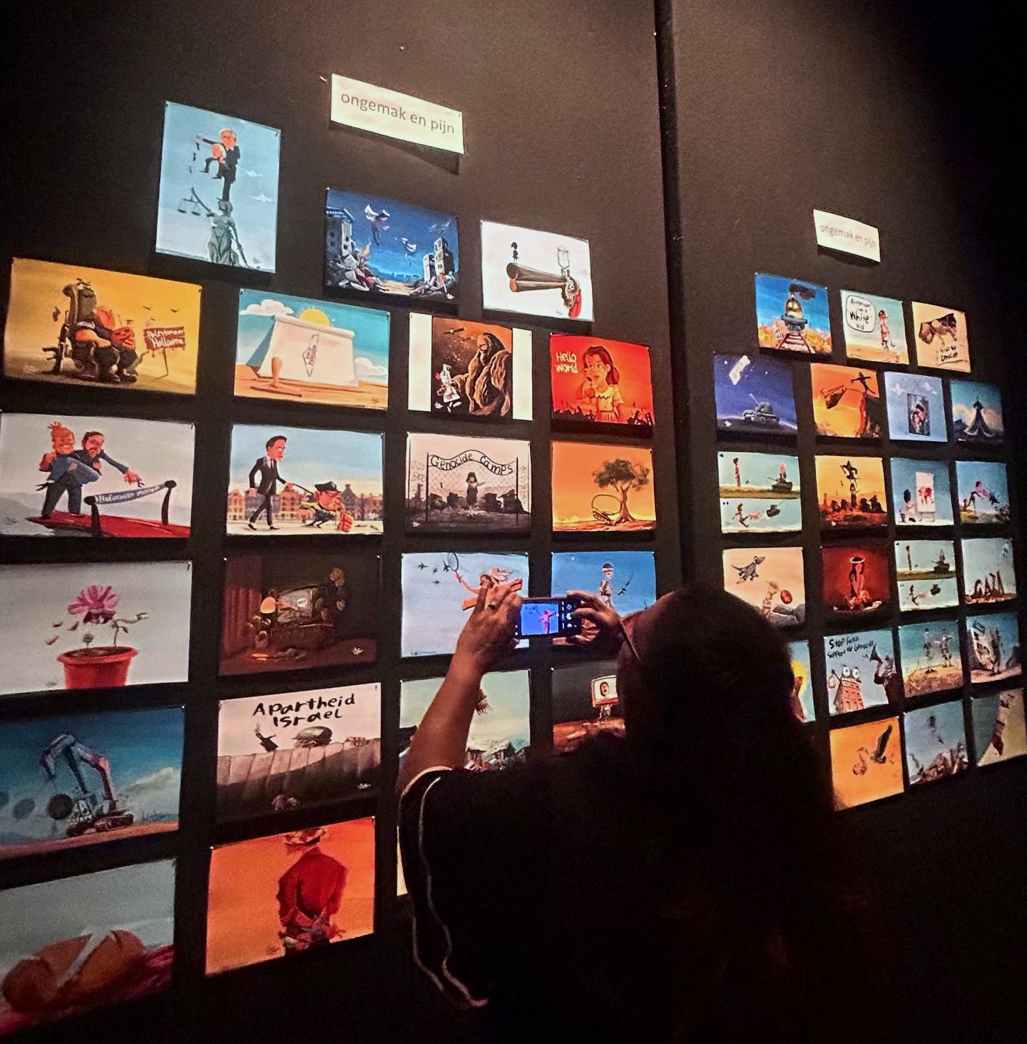 Een zwarte, stoffen wand met daarop afbeeldingen in een raster geprikt. Iedere afbeelding is een illustratie van de genocide, zionistische apartheid en misdaden, of misdaden, geweld en machtsmisbruik in Nederland.