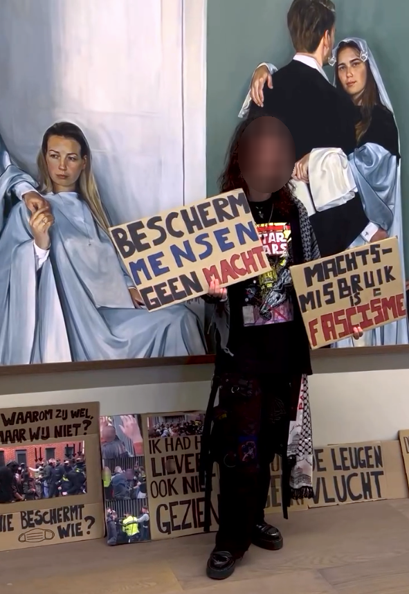 Een persoon staat in een galerie-achtige omgeving direct voor een groot schilderij. In hun hand en op de grond staan kartonnen borden met daarop teksten waaronder: 'Bescherm mensen, geen macht', 'Machtsmisbruik = fascisme', 'Waarom zij wel, maar wij niet? Wie beschermt wie?' (met een afbeelding van agenten in burger en met gezichtsmaskers), 'Ik had het liever ook niet gezien' (met afbeeldingen van politiegeweld).