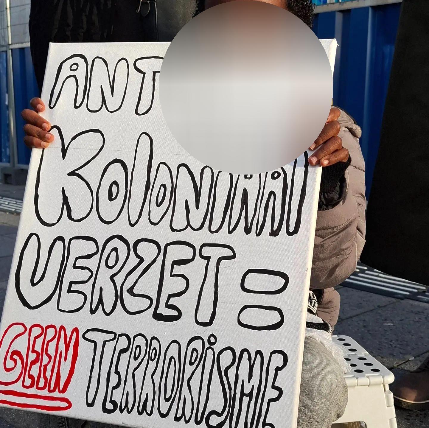 Een kind houdt een bord op met daarop de tekst: 'Anti-koloniaal verzet = geen terrorisme'.
